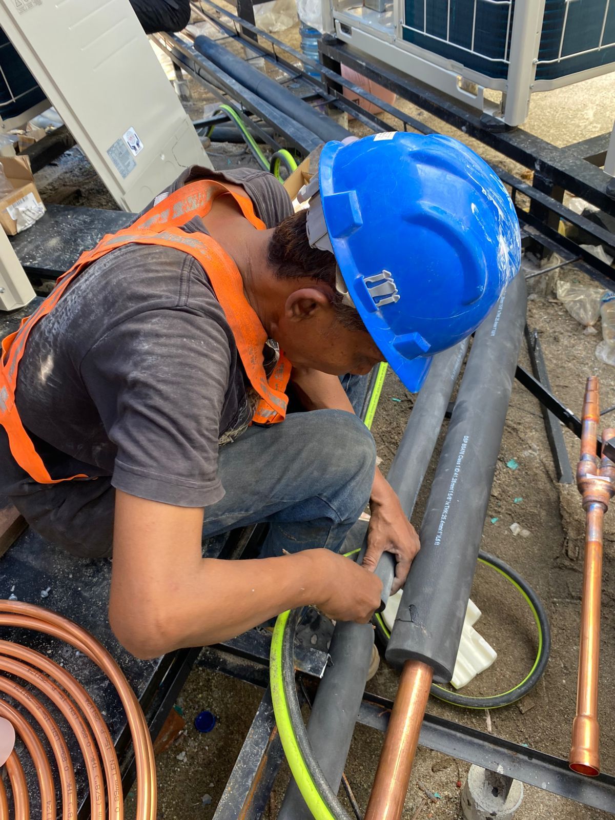 Teknisi berhelm menyambung pipa tembaga berinsulasi