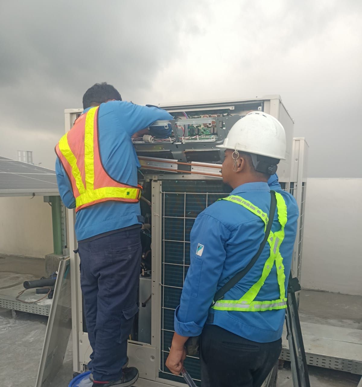 Dua teknisi memeriksa panel kontrol outdoor unit VRV di atap